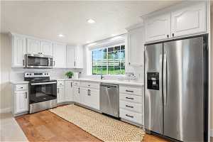 Kitchen with light hardwood / wood-style floors, backsplash, white cabinets, sink, and stainless steel appliances