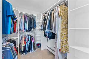 Walk in closet with a baseboard heating unit and light colored carpet