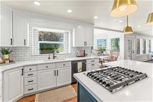 Kitchen with white cabinetry, light wood-type flooring, hanging light fixtures, dishwasher, and sink