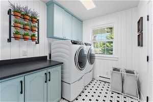 Clothes washing area featuring washer and dryer, baseboard heating, light tile floors, and cabinets