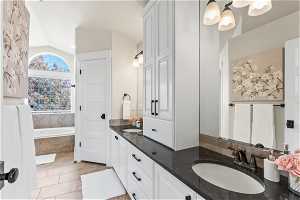 Bathroom featuring vaulted ceiling, double sink vanity, tile floors, and tiled tub