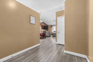 Corridor with a textured ceiling, light hardwood / wood-style flooring, and lofted ceiling