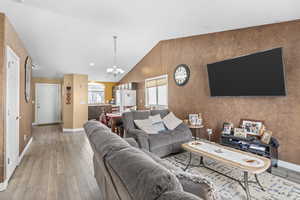 Living room with a chandelier, vaulted ceiling, and light hardwood / wood-style floors