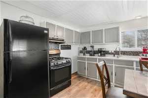 Kitchen featuring black appliances, light hardwood / wood-style floors, extractor fan, gray cabinets, and sink