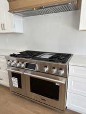 Kitchen featuring ventilation hood, double oven range, tasteful backsplash, and white cabinets