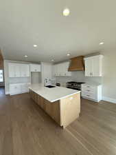 Kitchen featuring a sink, premium range hood, range with two ovens, baseboards, and wood finished floors