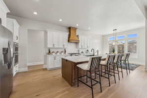 Kitchen with appliances with stainless steel finishes, light wood-type flooring, a sink, baseboards, and custom exhaust hood