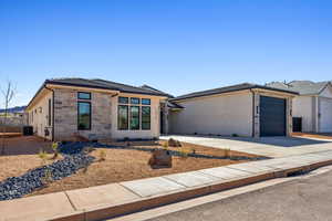 View of front of home featuring an attached garage, central AC, stone siding, stucco siding, and concrete driveway