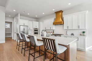 Kitchen with light wood-style flooring, premium range hood, stainless steel appliances, a large island, and recessed lighting