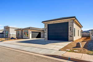View of front of home featuring a tile roof, concrete driveway, an attached garage, stone siding, and stucco siding