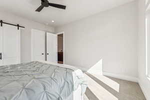 Carpeted bedroom with baseboards, a ceiling fan, and a barn door