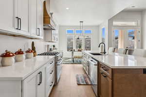 Kitchen featuring a sink, an island with sink, light wood-style flooring, stainless steel appliances, and custom range hood