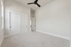 Unfurnished bedroom featuring a closet, baseboards, ceiling fan, light colored carpet, and vaulted ceiling