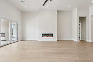 Unfurnished living room with visible vents, light wood-style floors, ceiling fan, and a glass covered fireplace
