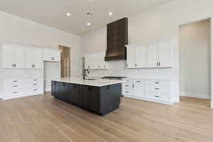 Kitchen featuring white cabinets, custom exhaust hood, a kitchen island with sink, and light countertops