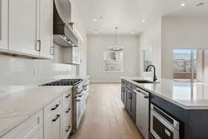 Kitchen featuring appliances with stainless steel finishes, a sink, light wood-style floors, visible vents, and custom exhaust hood