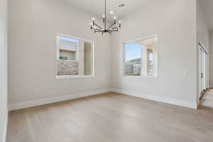 Empty room with baseboards, a notable chandelier, light wood-style flooring, and visible vents