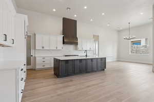 Kitchen with white cabinets, light wood finished floors, a chandelier, and premium range hood