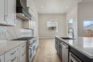 Kitchen featuring appliances with stainless steel finishes, a sink, light wood-style flooring, premium range hood, and decorative light fixtures