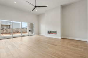 Unfurnished living room with a glass covered fireplace, baseboards, ceiling fan, light wood-type flooring, and recessed lighting