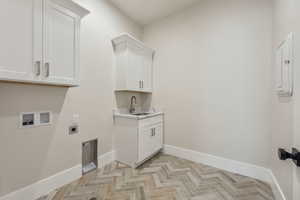 Washroom featuring electric dryer hookup, cabinet space, a sink, baseboards, and hookup for a washing machine