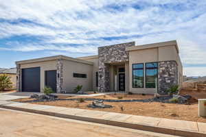 View of front of house featuring an attached garage, driveway, stone siding, and stucco siding