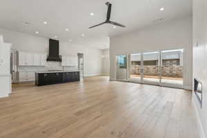 Unfurnished living room featuring recessed lighting, a towering ceiling, ceiling fan with notable chandelier, and light wood-type flooring