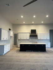 Kitchen with a spacious island, premium range hood, white cabinetry, light wood-type flooring, and decorative backsplash