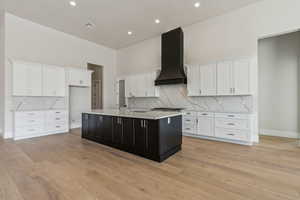 Kitchen with a sink, white cabinetry, an island with sink, and exhaust hood