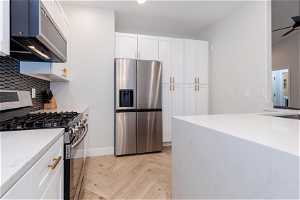 Kitchen with light parquet flooring, white cabinets, stainless steel appliances, ceiling fan, and tasteful backsplash