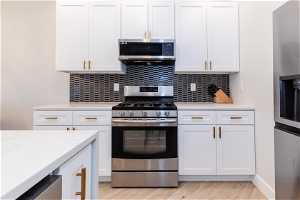 Kitchen featuring tasteful backsplash, white cabinets, light hardwood / wood-style floors, and stainless steel appliances