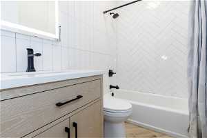 Full bathroom with toilet, vanity, tile walls, parquet flooring, and shower / bath combo