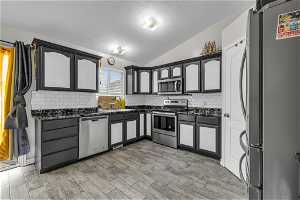 Kitchen featuring dark countertops, stainless steel appliances, backsplash, sink, and vaulted ceiling