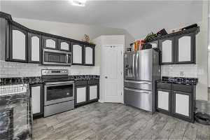 Kitchen featuring stainless steel appliances, tasteful backsplash, vaulted ceiling, and tile flooring.