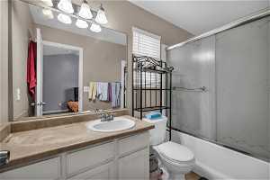 Full bathroom featuring toilet, large vanity, and combined bath / shower with glass door en-suit