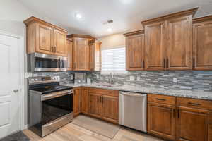 Kitchen featuring stainless steel appliances, light stone counters, backsplash, light hardwood / wood-style floors, and sink