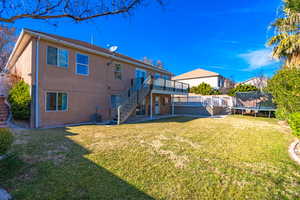 Back of house with a patio area, a yard, central AC unit, a trampoline, and a wooden deck