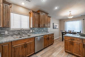 Kitchen featuring pendant lighting, dishwasher, light stone counters, and sink