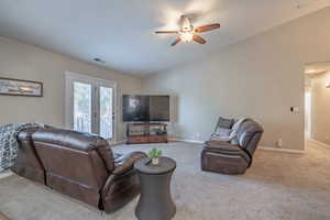 Living room with lofted ceiling, ceiling fan, light carpet, and french doors