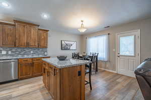 Kitchen with pendant lighting, light stone counters, a kitchen island, tasteful backsplash, and dishwasher