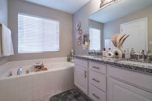 Bathroom with plenty of natural light, dual bowl vanity, and a relaxing tiled bath