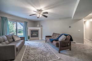 Carpeted living room featuring a fireplace, ceiling fan, and a textured ceiling