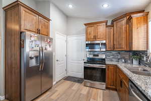 Kitchen with light hardwood / wood-style floors, backsplash, light stone countertops, vaulted ceiling, and appliances with stainless steel finishes