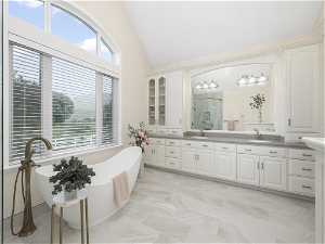 Master bathroom featuring double sink vanity, vaulted ceiling, tile floors, and independent shower and bath
