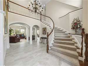 Stairs featuring a chandelier, light tile floors, crown molding, and ornate columns