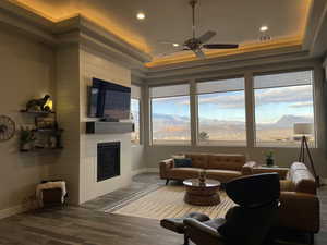 Living room featuring dark hardwood / wood-style flooring, a raised ceiling, ceiling fan, and a large fireplace