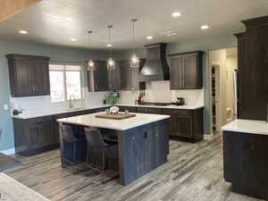 Kitchen featuring a kitchen island, custom exhaust hood, tasteful backsplash, a breakfast bar, and decorative light fixtures