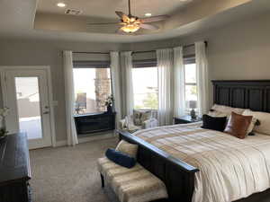 Carpeted bedroom featuring a tray ceiling and ceiling fan