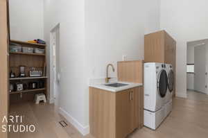 Laundry room with cabinets, light wood-type flooring, a high ceiling, sink, and washing machine and dryer