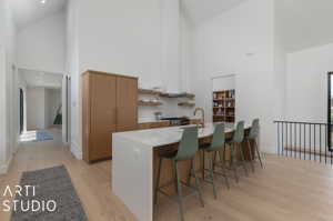 Kitchen with high vaulted ceiling, a kitchen breakfast bar, sink, and light hardwood / wood-style floors